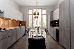 A modern kitchen with a glass dining table, grey cabinets, and a pendant light. - Luxury Family Home with Garden in West Kensington - 2 Mins to Tube - Pass the Keys (Londonderry)