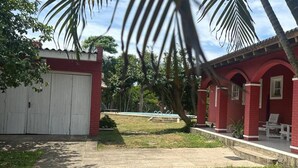 A red building with a white garage door, a pool, and palm trees.