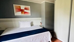 A hotel room with a bed, a nightstand, a white wardrobe, and a wall painting.