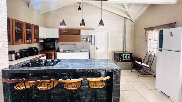 A kitchen with a marble island, wooden chairs, pendant lights, and a refrigerator.