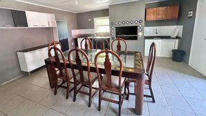 A dining area with a glass-top table and wooden chairs, a kitchen with cabinets and a microwave, and a tiled floor.
