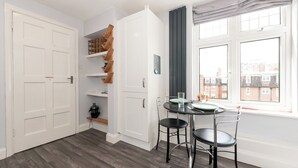 A room with a dining table, chairs, a white door, and a window with a view of buildings. - Riverside Serenity near Kingston and Hampton Court - Pass the Keys (Surbiton)