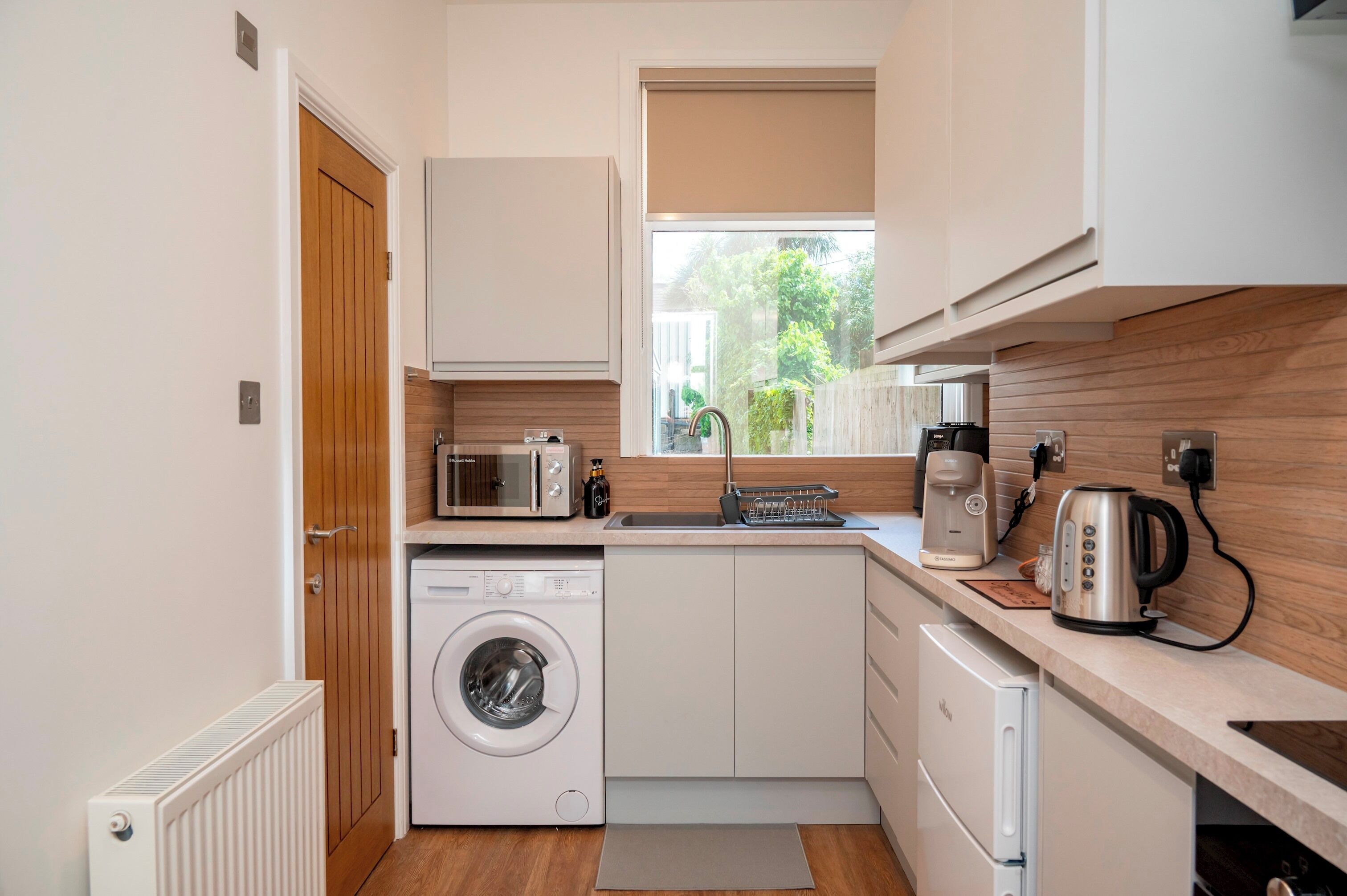 A compact kitchen with a washing machine, microwave, and coffee maker.