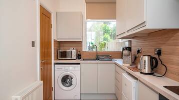A compact kitchen with a washing machine, microwave, and coffee maker.