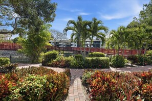A garden pathway leading to a building with a red bridge, surrounded by various plants and trees. - B-115 - Totally Updated - First Floor- Sleeps 6 (Naples)