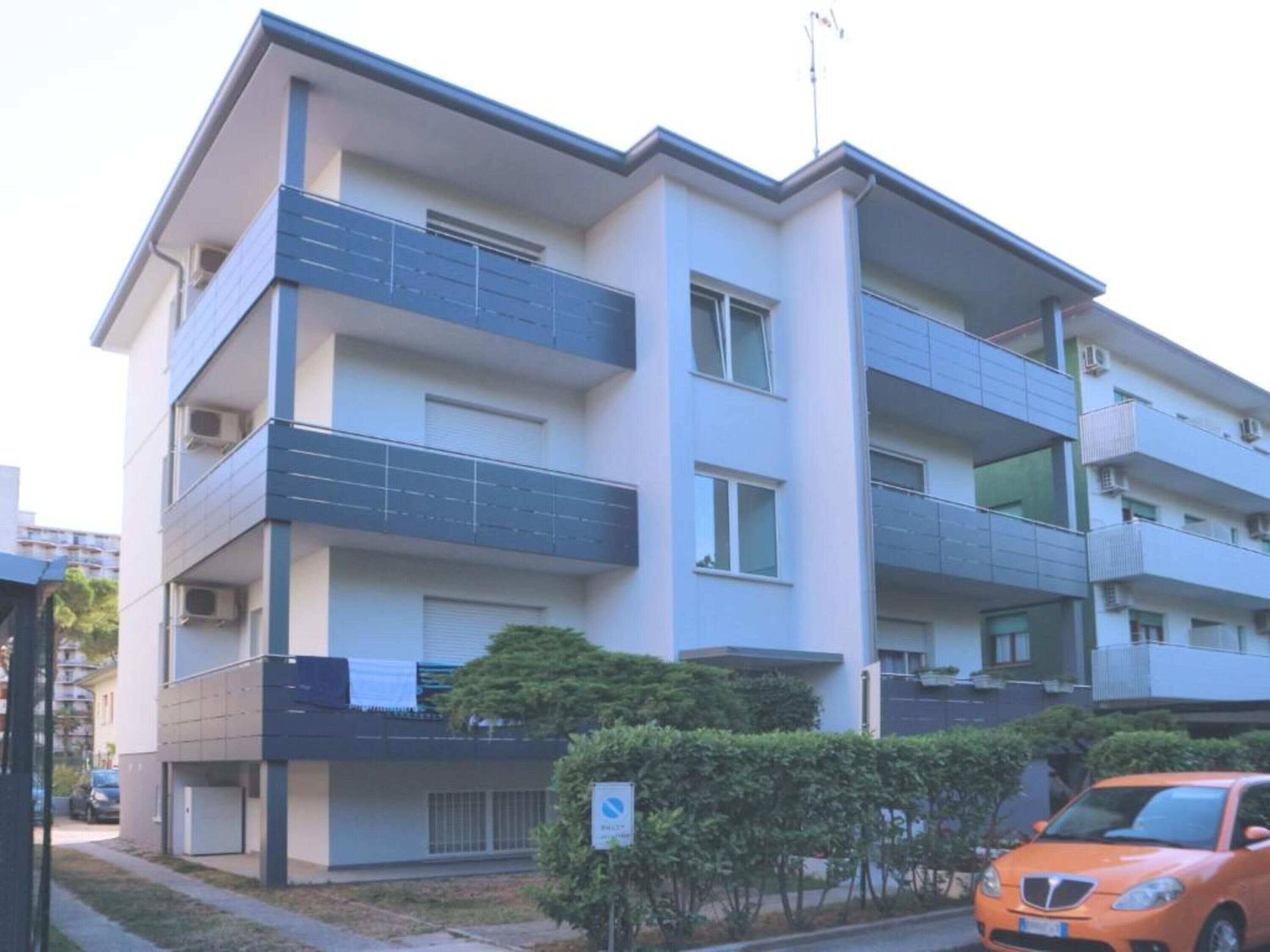 Um edifício residencial com várias andares, varandas, aparelhos de ar condicionado e uma área de estacionamento com um carro.
