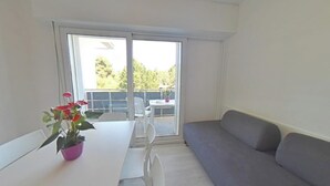 Una habitación con una mesa blanca, un sofá gris y un ventanal corredera que da a un espacio exterior con una mesa y sillas.