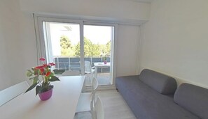 Ein Zimmer mit einem weißen Tisch, einem grauen Sofa und einer Glastür, die zu einem Außenbereich mit Tisch und Stühlen führt.
