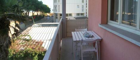 Ein Balkon mit Tisch und Stühlen, Blick auf ein Gebäude und einen Baum.