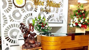 Uma mesa de recepção com um relógio, uma estátua de Buda e um arranjo floral.