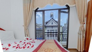 Quarto com cama, varanda e vista para uma casa, com cortinas.