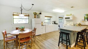 A kitchen with white cabinets, a dining table with chairs, a hanging light fixture, and a large island with stools. - River`s Edge Retreat (McComb)