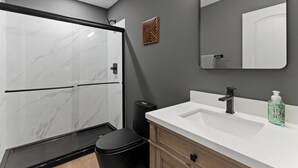 Een moderne badkamer met een douchecabine van glas, een wit wastafelmeubel en een houten opbergkast.
