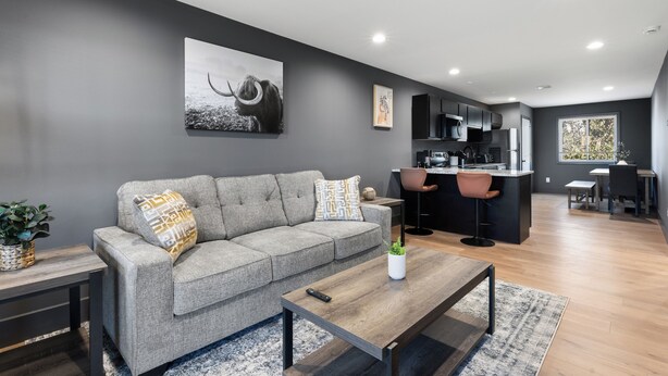 Een moderne woonkamer met een grijze bank, een salontafel en een keuken op de achtergrond.