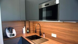 A modern kitchen with a built-in oven, a stainless steel sink, and a coffee maker. - Renovated 2-room apartment 30 m from the beach - Le Mourillon (Toulon)