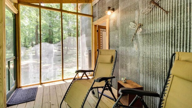 A room with large windows, a wooden ceiling, and two reclining chairs.