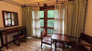 Una stanza con una scrivania in legno, una sedia, un tavolo, uno specchio e una finestra con tende.