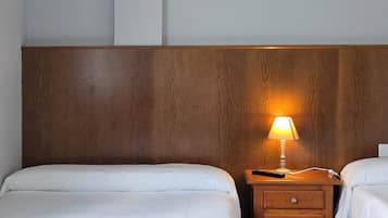 A hotel room with two beds, a wooden headboard, a nightstand with a lamp, and a drawer.