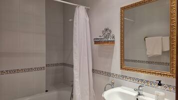 Un baño con bañera, ducha, lavamanos blanco y un espejo grande y decorativo.