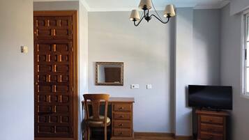 Une pièce comprenant une armoire en bois, un bureau avec une chaise, une télévision et un lustre.