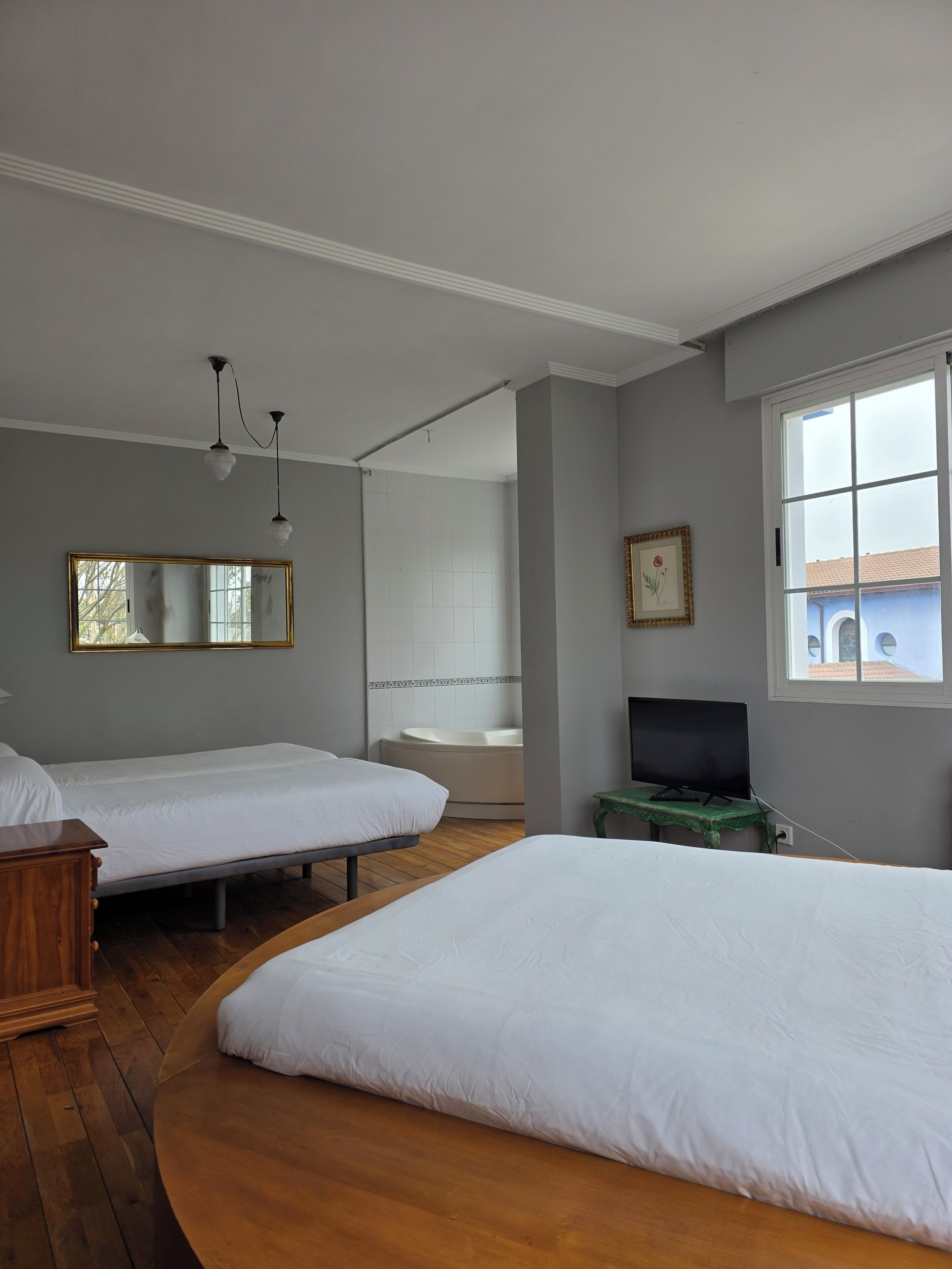 Een kamer met twee bedden, een badkuip, een televisie op een tafeltje en een raam.