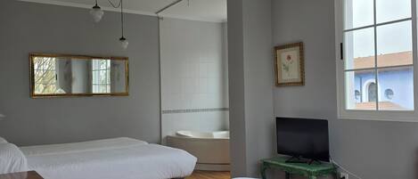 Een kamer met twee bedden, een badkuip, een televisie op een tafeltje en een raam.