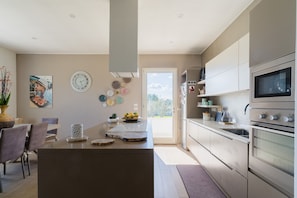 Une cuisine moderne dotée d’un îlot central, d’appareils électroménagers en acier inoxydable et offrant une vue à travers la porte.