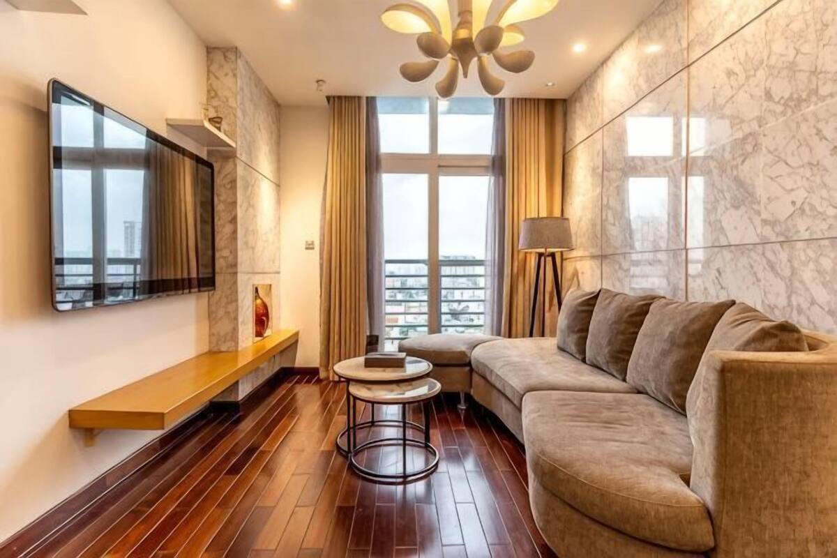 Un salon moderne avec un canapé, une table basse, un téléviseur fixé au mur et une grande fenêtre avec des rideaux.