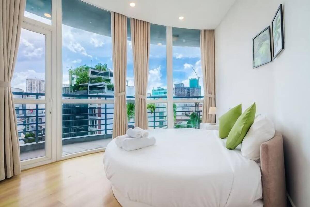 Une chambre avec un grand lit, une vue sur la ville grâce à de grandes fenêtres et un balcon.