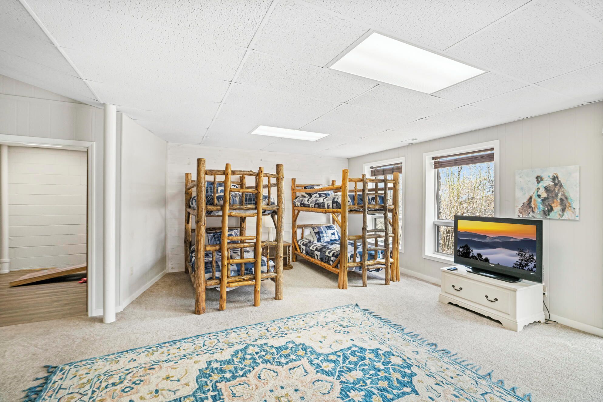 Ein Zimmer mit Etagenbetten, einem Fernseher, einem Gemälde und einem Fenster.