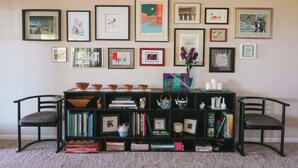 Quarto com estante preta, duas cadeiras e parede decorada com quadros.