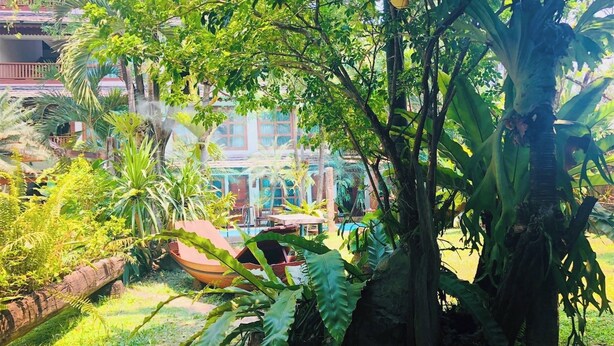 A lush garden with a pool, a wooden deck, and a building with a red roof in the background. - Room-302 Serene Teak Boutique Apartments (Chiang Mai)