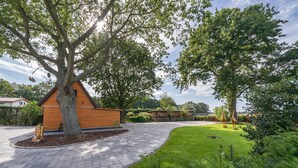 Un patio empedrado con un árbol grande, una estructura de madera y un césped bien cuidado.