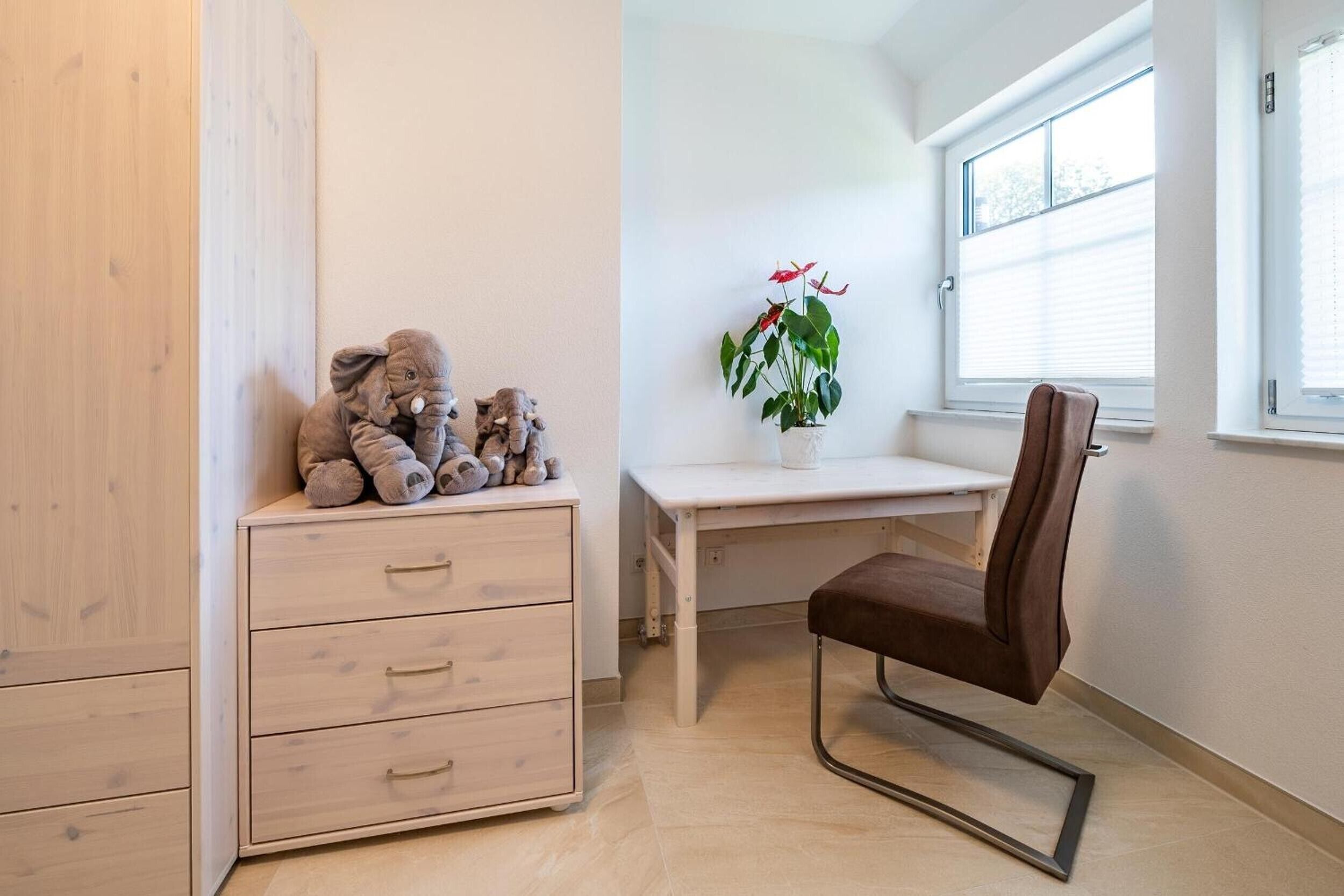 Una habitación con un armario de madera, un escritorio con silla, una planta en maceta y un ventanal.