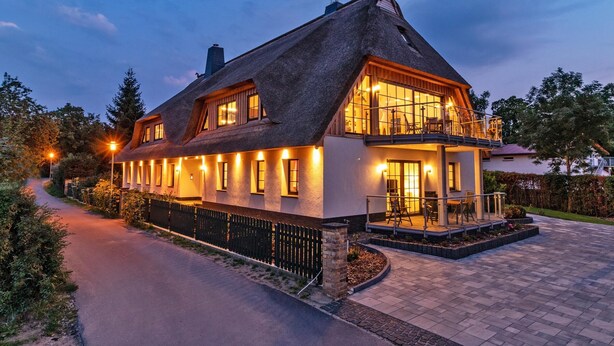 Een groot huis met rieten dak, een balkon en een verharde oprit.