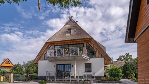 Ein zweistöckiges Gebäude mit einem geneigten Dach, einem Balkon im oberen Geschoss und einem gepflasterten Innenhof.