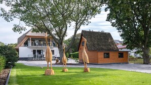 Ein modernes Haus mit einem großen Rasen, einer Holzskulptur und einem Gebäude mit einem Reetdach.