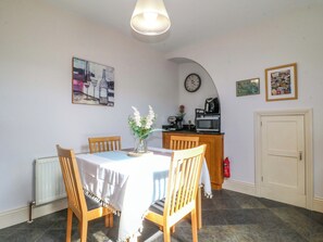 A dining area with a table, chairs, a vase of flowers, a clock, and a kitchen area with a microwave. - 2A Water Street (Bakewell)