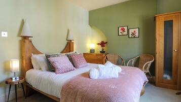 Una cama bien hecha con almohadas, una lámpara de noche, una mesita con lámpara, una silla y un armario en una habitación con paredes verdes.