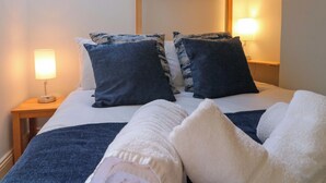 Una cama con dos almohadas, una mesita de noche con lámpara y una estructura de techo de madera.