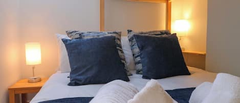 Una cama con dos almohadas, una mesita de noche con lámpara y una estructura de techo de madera.