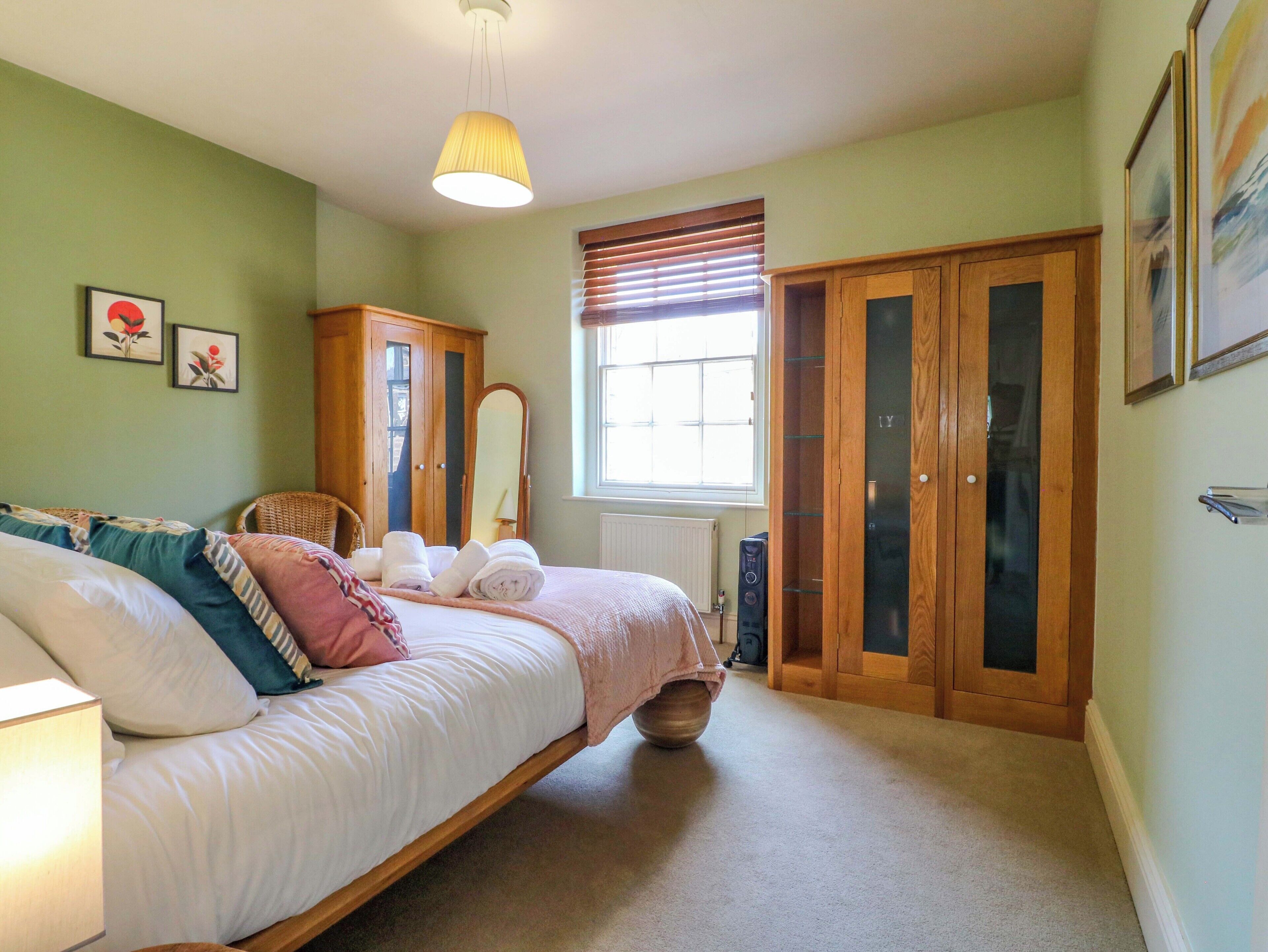 Un dormitorio con cama, armario de madera, espejo y ventana con persianas.