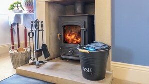 Una habitación con chimenea, una cesta, un cubo metálico con la etiqueta 'ASH' y una mesa cubierta con un mantel azul.