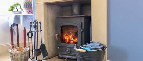 A room with a fireplace, a basket, a metal bucket labeled 'ASH,' and a table with a blue tablecloth.