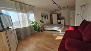 Une chambre à coucher moderne avec un lit, un canapé rouge, une télévision, une bibliothèque et une plante en pot.