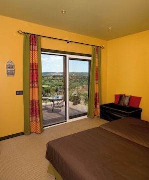 A hotel room with a bed, a small table, and a view of a green landscape through a sliding door. - 'silves' Cabin-cato Preto-adults-only Guesthouse (Silves)