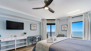 Une chambre avec un lit, un bureau, une chaise, un téléviseur à écran plat et un balcon offrant une vue sur la mer.