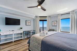 A bedroom with a bed, a desk, a chair, a flat-screen TV, and a balcony with a view of the sea. - South Wind 1206 - Oceanfront Condo with Amazing Views! (Myrtle Beach)