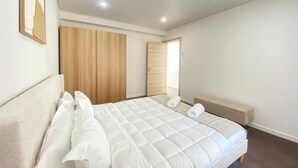 Un dormitorio con cama, armario de madera, banco y puerta que da a otra habitación.