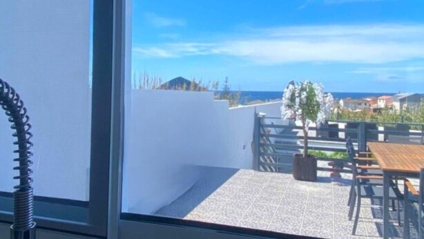Un balcón con vista al mar, una pared blanca y mobiliario exterior.